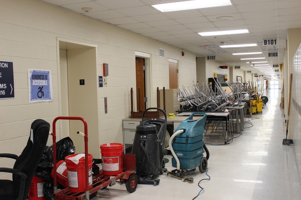 Image of school hallway with desks, vacuums, and maintenance equipment. 